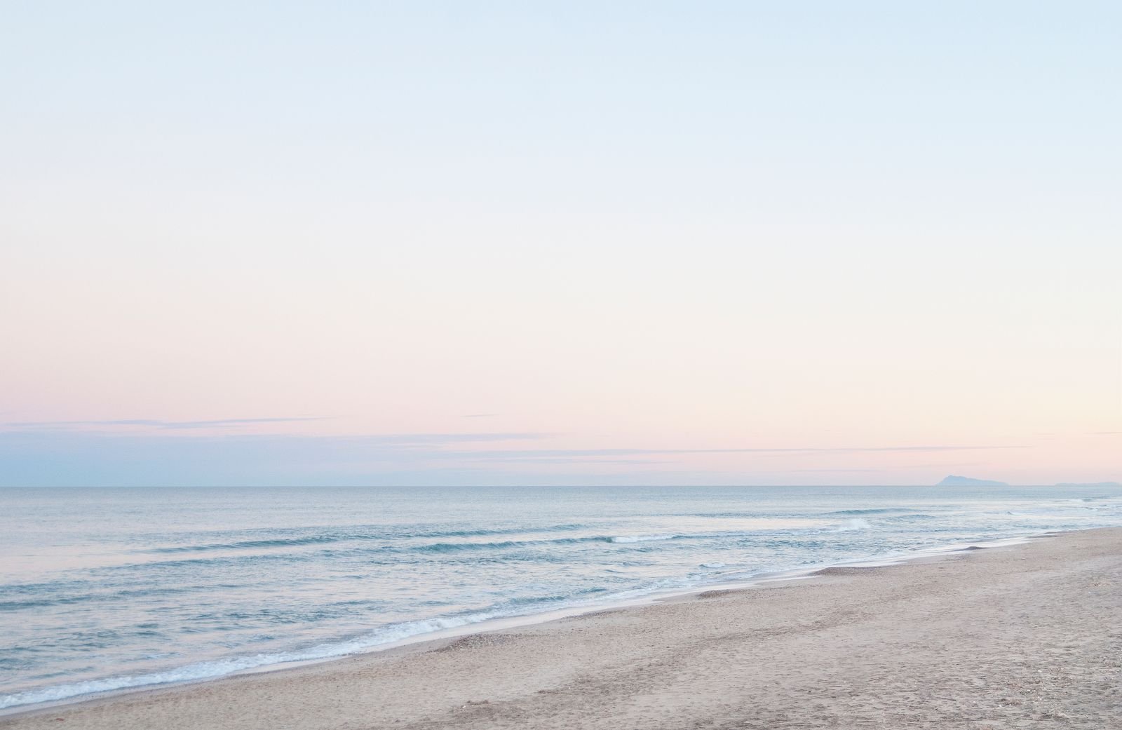 A calm shoreline at first light, pale sky meeting still water