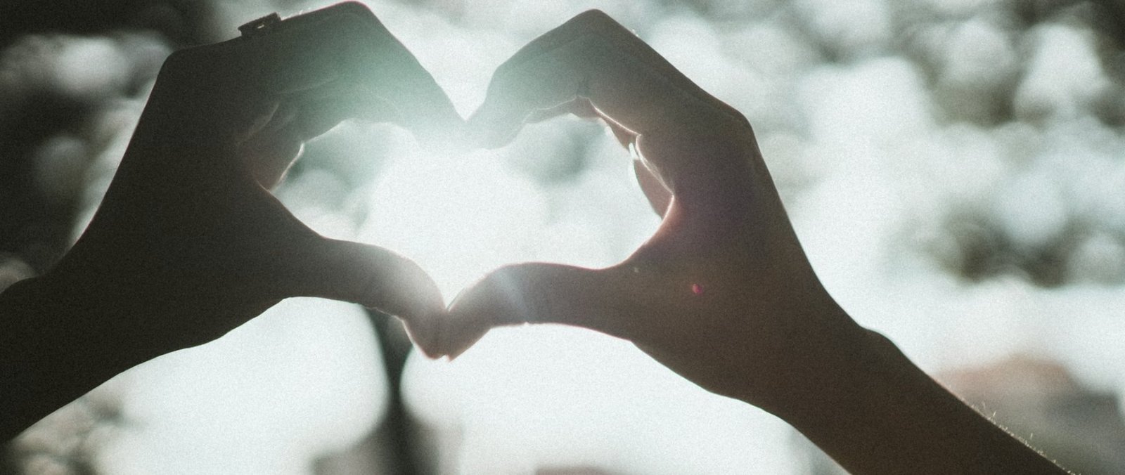 Two hands forming a heart shape with sunlight shining through